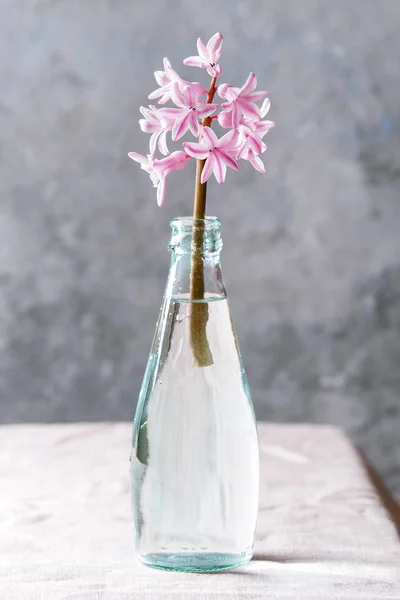 在桌上放着亚麻桌布的蓝色玻璃瓶里盛开的粉红色风信子 — 图库照片