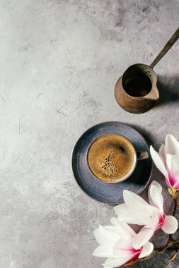 Gri doku arka plan üzerinde siyah espresso kahve, vintage jezva ve bahar çiçekleri Manolya mavi kupa dalları. Üstten Görünüm alanı. Bahar tebrik kartı