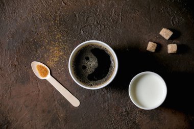 Kağıt bardakta americano kahvesi ve süt, geri dönüşümlü tahta kaşık şeker ve koyu dokuya sahip arka plan. Düz uzanış, boşluk