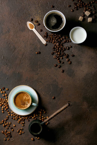 Variety of paper cups of americano coffee and milk versus turkish coffee in ceramic cup and cezve, recycled wooden spoon of cane sugar, coffee beans over dark texture background. Flat lay, space