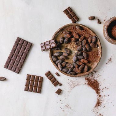 Koyu ve çikolatalı çikolata, kakao çekirdekleri, beyaz mermer arka planda seramik kasede kakao tozu. Düz uzanış, boşluk