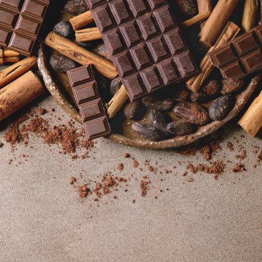 Koyu ve sütlü çikolata ve kakao çekirdeği ile doğranmış kakao tozu ve tarçın çubukları seramik palette kahverengi doku üzerinde. Düz uzanış, boşluk