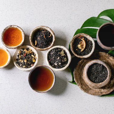 Geleneksel ve wabi sabi tarzı fireclay seramik bardak ve kâselerde gri benekli arka planda egzotik canavar yaprağı üzerinde çeşitli sıcak ve kuru çay çeşitleri. Düz uzanış, boşluk