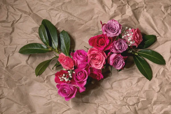 创意布局与美丽的粉红色玫瑰花和绿色叶子在皱巴巴的手工纸背 平躺在床上贺卡概念 — 图库照片
