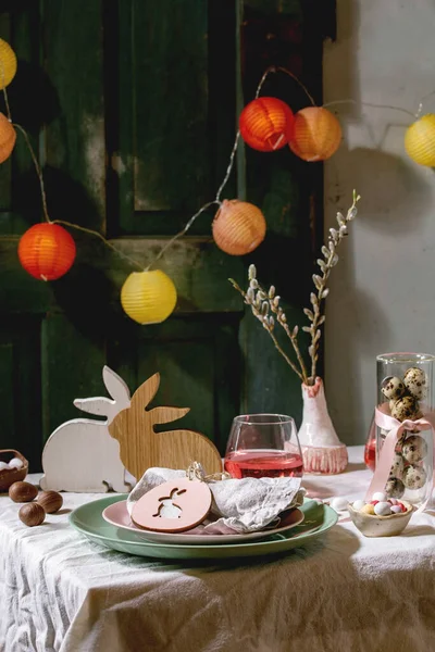 复活节桌上摆满了木兔装饰 巧克力蛋和糖果 粉色鸡尾酒饮品 白色桌布上的空盘子 照明的花环 假日晚餐 — 图库照片