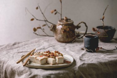 Japon usulü ipek tofu soya peyniri dilimlenmiş küp kırmızı biber, soğan ve soya sosu seramik tabakta yemek çubukları, seramik çaydanlık ve gri keten masa örtüsünde bardaklar. Asya yemeği.