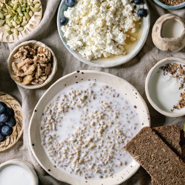 Sağlıklı kahvaltı. Çeşitli kahvaltı yemekleri, buğday, yoğurt, kefir, süzme peynir, avokado, çavdar ekmeği, tohum, fındık ve böğürtlen çeşitleri seramik kaselerde. Keten kumaş arka plan. Düz yatıyordu