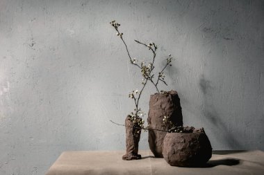 Gri masa örtüsünün üzerindeki kil vazolarda çiçek açan kiraz dalları. Bahar iç dekorasyonları.