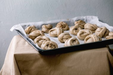 Geleneksel İsveç kakule tatlı çörekleri pişirmeye hazır fırın tepsisi üzerinde kanelbulle Gri keten masa örtüsü üzerinde kağıt pişirerek.