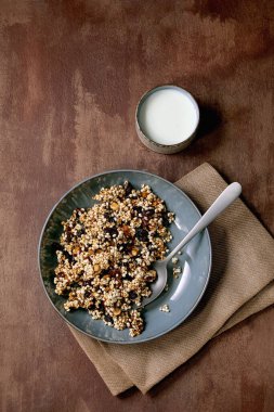 Ev yapımı çıtır çıtır darı taneli, kurutulmuş meyve taneli ve tekstil peçetesinde seramik tabakta fındıklı kahverengi dokuda bir fincan yoğurt. Düz uzanış, boşluk. Sağlıklı kahvaltı.