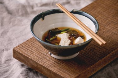 Japon Miso çorbası, ipek tofu küpleri, soya fasulyesi edamame, yeşil fasulye geleneksel kâse içinde çubuklarla ahşap Japon sofrasında gri keten masa örtüsü. Asya yemeği.