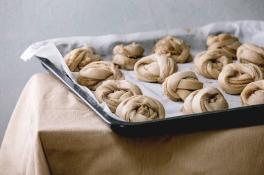 Geleneksel İsveç kakule tatlı çörekleri pişirmeye hazır fırın tepsisi üzerinde kanelbulle Gri keten masa örtüsü üzerinde kağıt pişirerek.