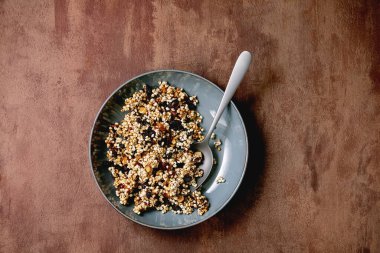 Ev yapımı gevrek darı gevreği, kurutulmuş meyve taneleri ve kahverengi desenli seramik tabakta fındıklar. Düz uzanış, boşluk. Sağlıklı kahvaltı.