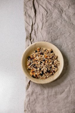 Ev yapımı gevrek darı gevreği, kurutulmuş meyve taneleri ve beyaz arka planda gri keten kumaş üzerinde seramik kasede fındıklar. Düz uzanış, boşluk. Sağlıklı kahvaltı.
