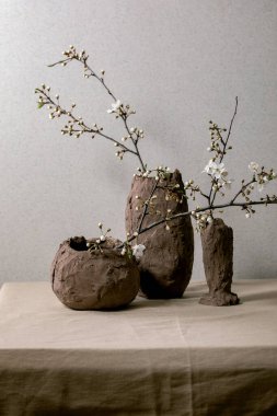 Gri masa örtüsünün üzerindeki kil vazolarda çiçek açan kiraz dalları. Bahar iç dekorasyonları.
