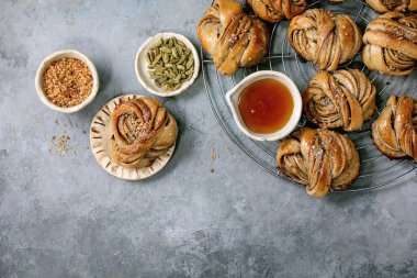 Geleneksel İsveç kakule tatlı çörekleri soğutma rafında, seramik kasenin içindeki malzemeler gri beton desenli arka planda. Düz uzanış, boşluk