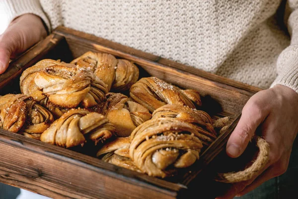 伝統的なスウェーデンのカルダモンやシナモンの甘いパンを作った家で手木製のトレイで保持ベージュニットセーターの女性Kanelbulle — ストック写真