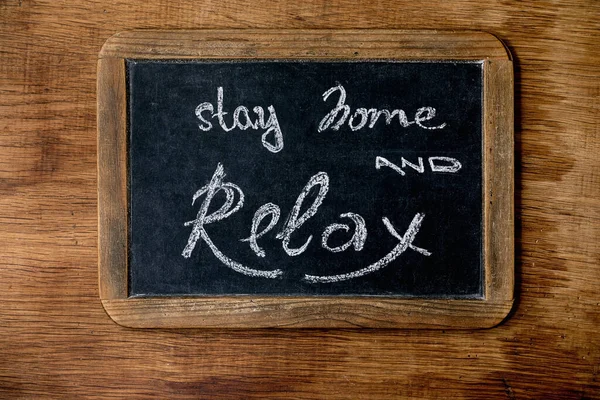 Stay home quarantine isolation period concept. Vintage chalkboard with handwritten chalk lettering Stay home and relax. Wooden background