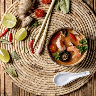 Geleneksel baharatlı Tayland çorbası Tom yum kung Shiitake mantarı ve karidesli, saman hasırından peçetenin üzerindeki malzemeler ahşap arka planda. Düz uzanış, boşluk