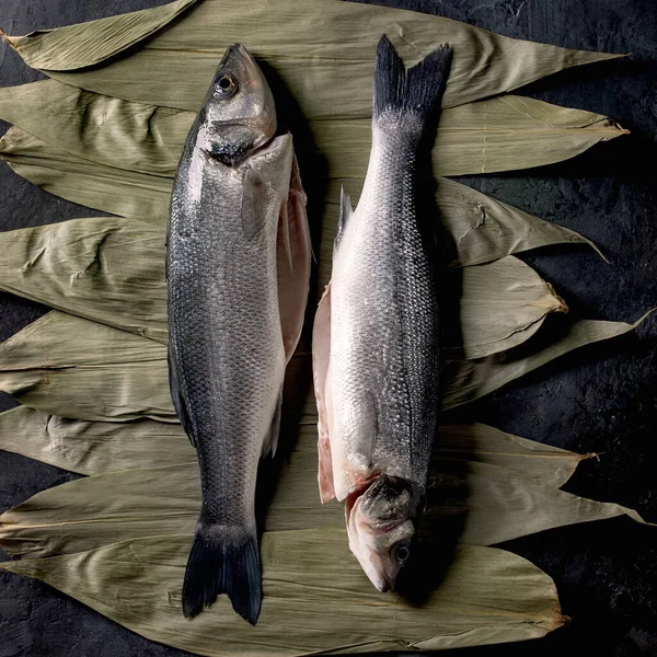 乾燥した竹の葉の2つの生の新鮮な調理されていない魚のベースは 暗い質感のコンクリートの背景に調理する準備ができています — ストック写真