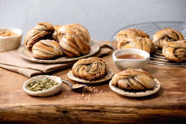 Geleneksel İsveç kakule tatlı çörekler tabakta Kanelbulle, seramik kasedeki malzemeler ahşap masanın üstünde..