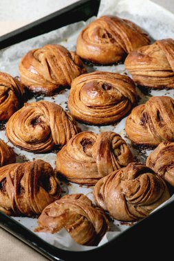 Taze fırınlanmış geleneksel İsveç tarçını tatlı çörekler fırın tepsisi üzerinde kanelbulle bej keten masa örtüsü üzerinde kağıt pişirerek.