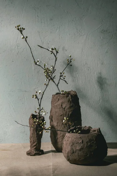 在灰色桌布上的不同工艺粘土花瓶中的花樱桃分枝 春天室内装饰 — 图库照片