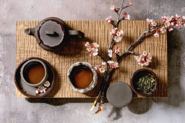 Tea drinking wabi sabi japanese style dark clay cups and teapot on wooden tea table with blooming cherry branches. Grey texture concrete background. Flat lay, space clipart