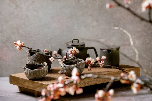 茶喝的是日本风格的芥末砂浆杯和茶壶 放在开着樱花枝条的木制茶几上 灰色纹理混凝土背景 — 图库照片