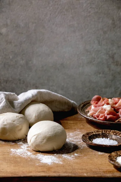 イタリアのピザのナポリ料理のための生地 木製のキッチンテーブルの上にセラミックプレート上に新鮮な自家製小麦生地 プロシュートと材料の3つのボール ホームベーキング — ストック写真
