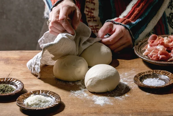編んだセーターの女性はイタリアのピザのナポリを調理します 木製のキッチンテーブルの上にセラミックプレート上に新鮮な自家製小麦生地 プロシュートと材料の3つのボール ホームベーキング — ストック写真