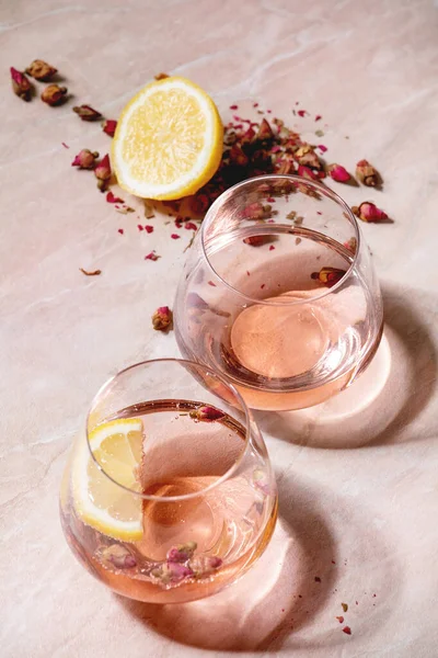 ピンクのバラのシャンパン サイダーまたはレモネードのカクテルグラスにドライローズの芽とレモン ピンク大理石の背景 — ストック写真