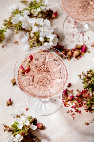 ピンク色のバラのシャンパン サイダーまたはレモネードのクリスタルグラス 上の桜の枝 ピンク大理石の背景 — ストック写真