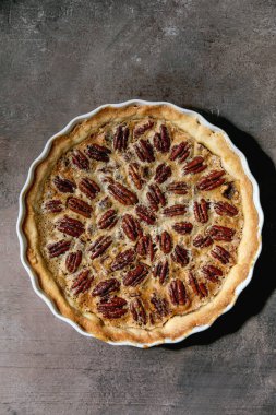 Taze ev yapımı klasik Amerikan cevizli turta, beyaz seramik fırın kabında, gri doku arka planında. Düz uzanış, boşluk