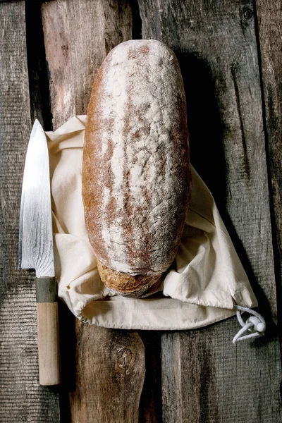 全粒穀物焼きたての職人ライ麦 綿繊維袋から有機パン 古い木製の背景に大きなナイフ — ストック写真