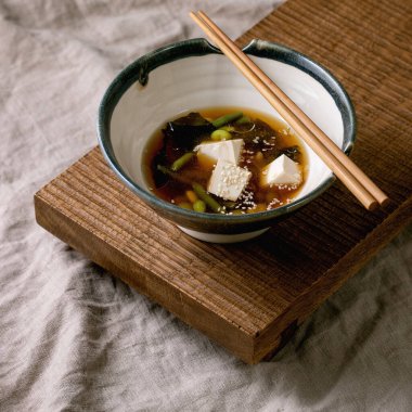Japon Miso çorbası, ipek tofu küpleri, soya fasulyesi edamame, yeşil fasulye geleneksel kâse içinde çubuklarla ahşap Japon sofrasında gri keten masa örtüsü. Asya yemeği.