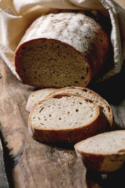 Pamuk tekstil torbasından dilimlenmiş tahıllı çavdar-buğday organik ekmeği eski ahşap arka planda. Kapat.