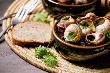 Salyangoz de Bourgogne - tereyağlı salyangoz, gurme yemeği, iki geleneksel seramik tavada kişniş ve saman peçetesinde ekmek. Kapat.
