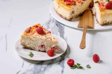 Taze ahududu, nane, nane ve ahşap kek sunucusuyla süslenmiş, beyaz mermer zemin üzerine dilimlenmiş ev yapımı ahududu pişmiş peynirli kek..