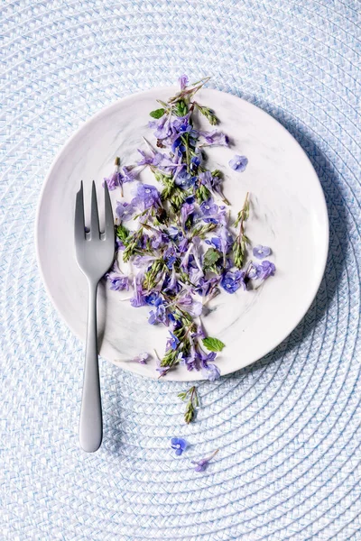 Fioletowe Purpurowe Jadalne Kwiaty Białym Talerzu Widelcem Deserowym Niebieskim Dzianinie — Zdjęcie stockowe