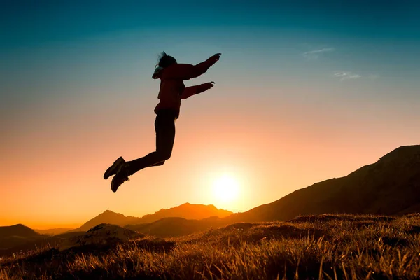 Chica salta en el prado durante una puesta de sol en las montañas — Foto de Stock