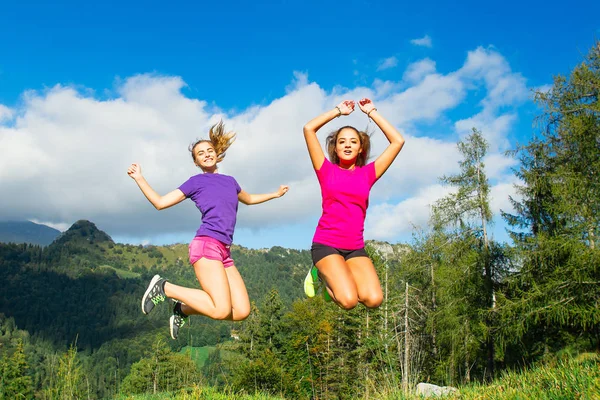 Zwei junge hübsche Mädchen springen auf dem Gras in einer Berglandschaft — Stockfoto