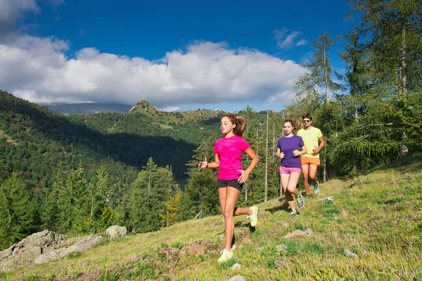 Due giovani ragazze sportive e un ragazzo che corrono insieme sull'erba i — Foto Stock