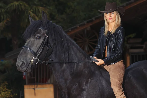 A beautiful blond girl over a black horse — Stock Photo, Image