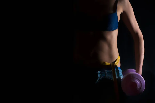 Girl with gym weights and centimeter at the waist on a black bac — Stock Photo, Image