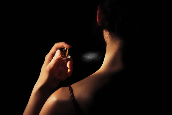 Mulher pulveriza perfume em seu pescoço com um fundo preto — Fotografia de Stock