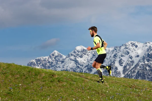 Skyrunning un hombre barbudo en un prado de primavera con montañas de nieve — Foto de Stock