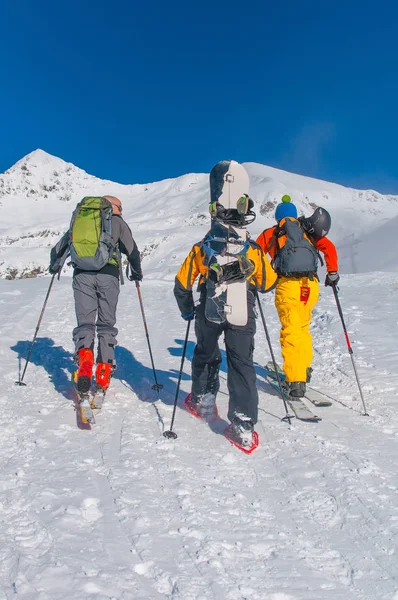 Przyjaciele z nart i snowboardów iść na wzgórze z rakietami śnieżnymi — Zdjęcie stockowe