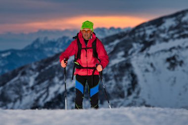 At sunset a ski touring uphill on the Alps clipart