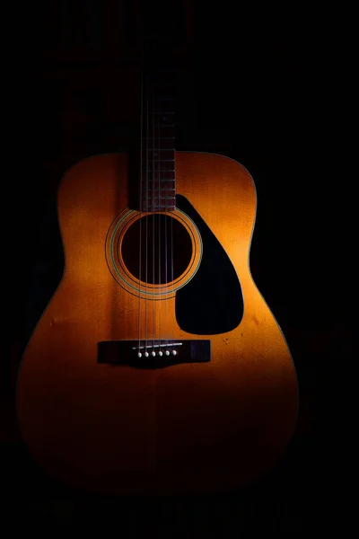 在光线或阴影之间的黑色背景上的声学吉他 — 图库照片